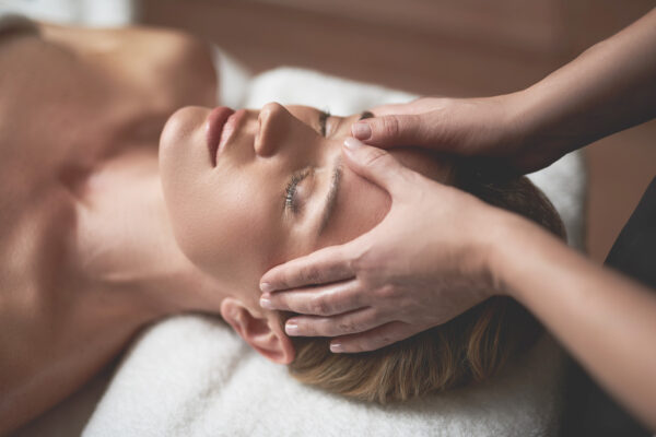 Concept of relaxation and body care. Top angle portrait of female therapist making anti-age massage of forehead wrinkles to young woman in spa salon